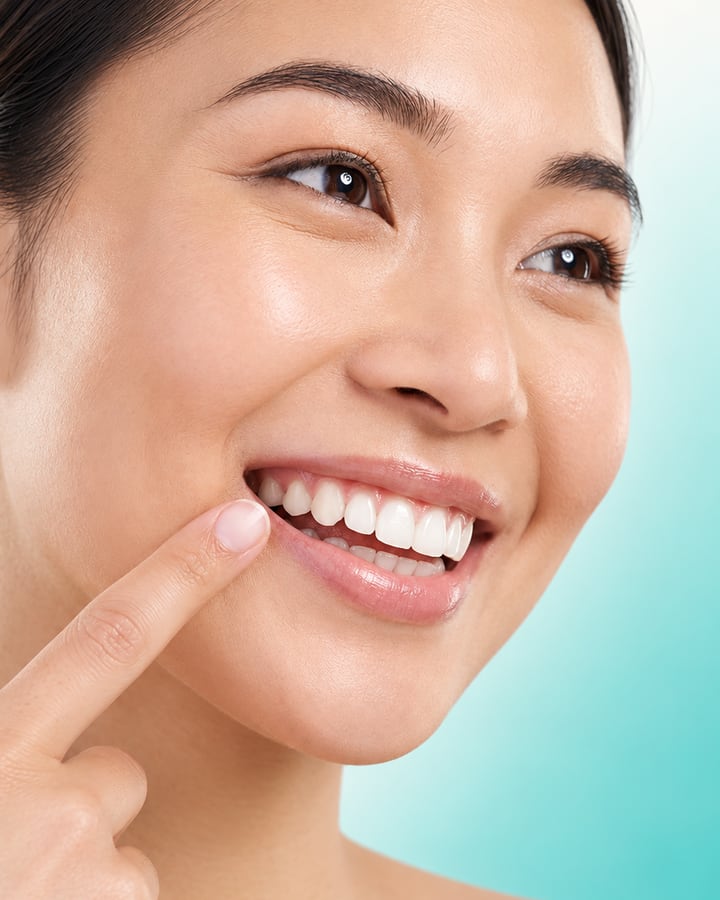Smiling patient pointing to a healthy, bright smile