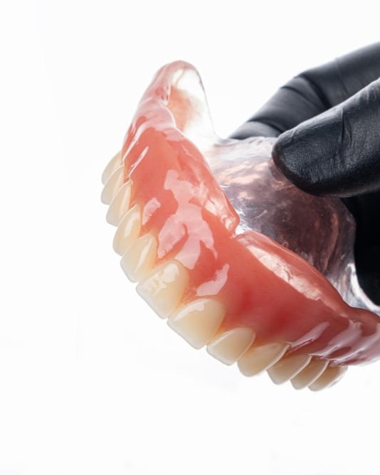A lower suction BPS denture held in a gloved hand at Dr Ray & Partners Dental