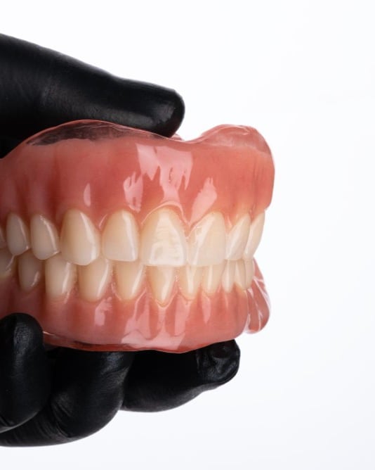 A full set of upper and lower BPS dentures held in gloved hands at Dr Ray & Partners Dental